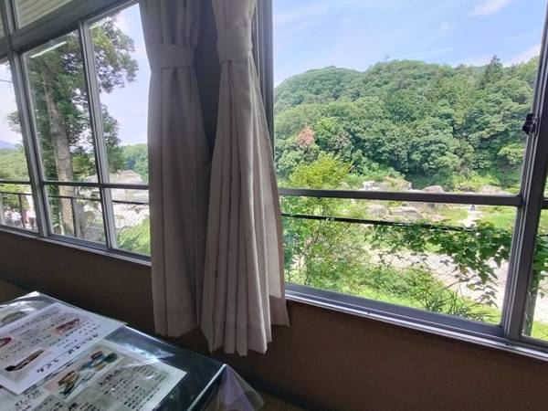 A scenic view of lush green mountains and the River seen through the window of Miharashi, a traditional Japanese restaurant in Nagatoro.